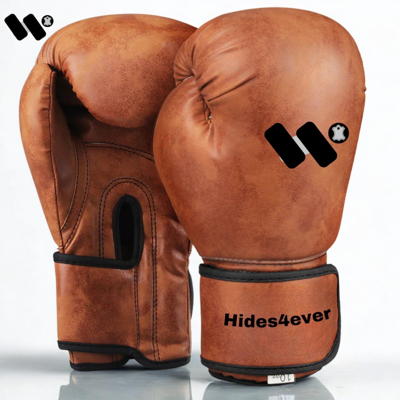 May include: A pair of brown leather boxing gloves with black trim. The gloves have a distressed, vintage look and feature the text "Hides4ever" on the wrist strap. The gloves are 10 oz.