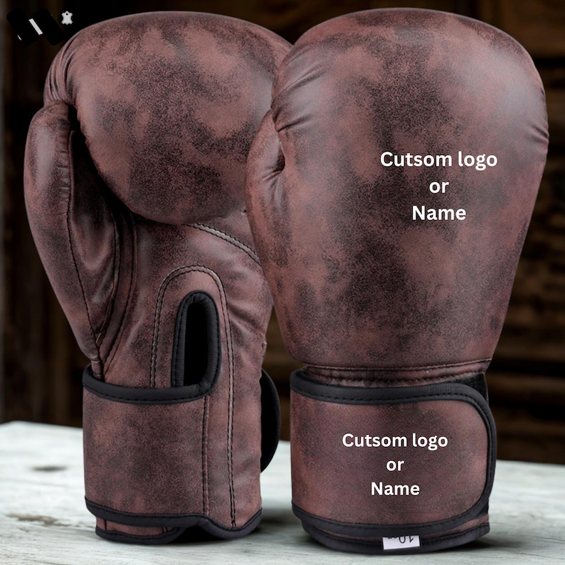May include: Pair of brown boxing gloves with a distressed leather appearance. The gloves have black wrist straps and the text "Cutsom logo or Name" is printed on the front. The gloves are designed for boxing or other combat sports.
