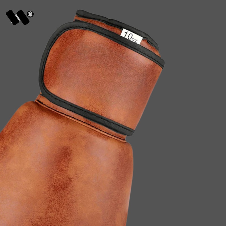 May include: Close-up of a brown leather boxing glove with black trim. The glove has a label that reads "10oz". The glove is designed for boxing and martial arts training.