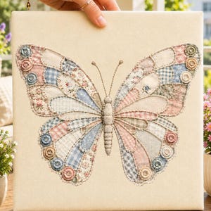 Op de afbeelding: Een vierkant canvas met een grote vlinderapplicatie gemaakt van diverse lapjes stof in zachte pasteltinten zoals roze, blauw en crème. De vlindervleugels zijn omlijnd met decoratief stiksel en geaccentueerd met kleine ronde stoffen knoopjes.