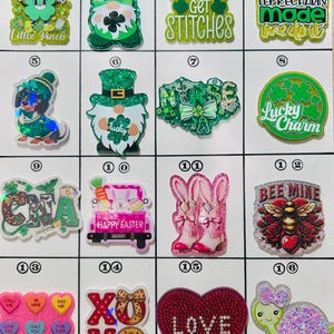May include: A collection of colorful, glittery resin charms with various designs. The charms include St. Patrick's Day themes like shamrocks and leprechauns, Easter bunnies, and Valentine's Day hearts and candies. Some charms have text like "Bee Mine" and "Love".