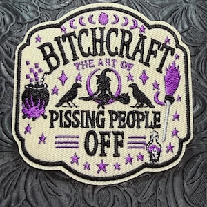 May include: An embroidered patch with a cream background and black border. It features purple and black thread designs including a cauldron, a witch on a broom, two ravens, a broomstick, and stars. Text reads: BITCHCRAFT THE ART OF PISSING PEOPLE OFF.