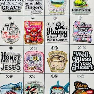 May include: A collection of 16 colorful acrylic charms with various humorous phrases and images. Designs include a frog, shark, cow, taco, and phrases like "Mind your own biscuits" and "Be Happy." These charms are suitable for shoes, bracelets, and other accessories.