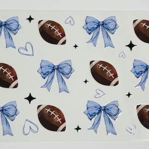 May include: A sheet of stickers with a repeating pattern of brown footballs, light blue bows, black star shapes, and white hearts. The footballs have white stitching.
