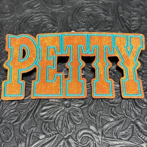 May include: A patch featuring the word PETTY in large, block-style letters. The letters are orange with a textured, glittery finish and are outlined with a bright teal border. The design has a bold, collegiate appearance with sharp edges.