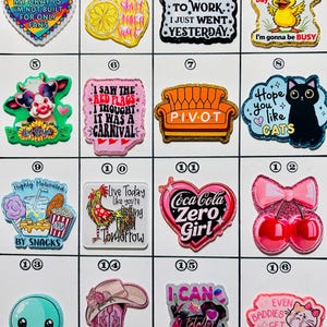 May include: A collection of colorful, decorative charms with various designs and text. Designs include a heart with text, a lemon, a quote, a duck, a cow, a couch, a cat, snacks, a rooster, a heart, cherries, an octopus, a cowboy boot, and a cat.