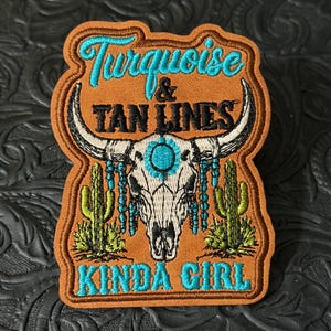 May include: An embroidered patch with a tan background featuring a white steer skull with turquoise accents, green cacti, and the text "Turquoise & TAN LINES KINDA GIRL" in turquoise and black lettering, with a brown stitched border.