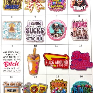 May include: A collection of colorful, glittery charms with various designs and text. Designs include a bow with strawberries, a skull with binoculars, and the text "I SAW THAT".
