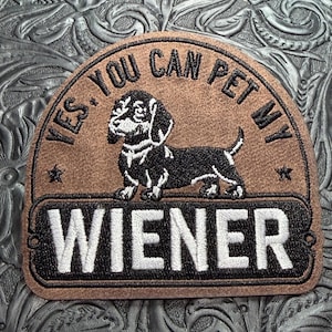 May include: A semi-circular brown patch featuring an embroidered black and white dachshund illustration. The text reads YES. YOU CAN PET MY WIENER in black and white lettering, with two small stars flanking the dog on the brown background.