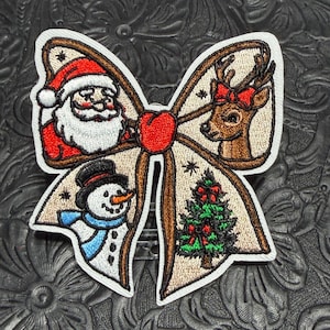 May include: A bow-shaped embroidered patch featuring four distinct holiday illustrations: a Santa Claus, a reindeer with a red bow, a snowman with a blue scarf, and a decorated Christmas tree, all centered around a solid red heart icon.