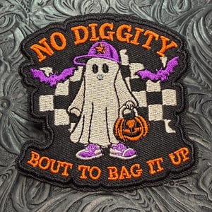 May include: An embroidered patch featuring a white ghost wearing a purple baseball cap and sneakers, holding an orange pumpkin bucket. The background has a black and white checkered pattern and purple bats. Text reads NO DIGGITY BOUT TO BAG IT UP.