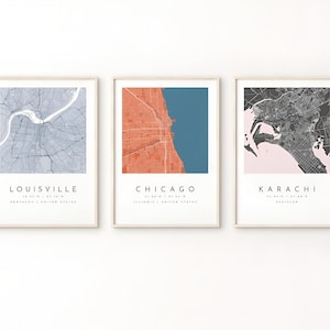 May include: Three framed vertical wall art prints featuring stylized city maps of Louisville, Chicago, and Karachi. Each print displays a unique color scheme, geographic street grid, and the city name with coordinates in a clean, sans-serif font.