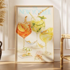 May include: A framed art print of a New Yorker magazine cover featuring watercolor illustrations of three large cocktail glasses filled with orange, green, and yellow drinks, with tiny figures lounging in and around the glasses on beach gear.