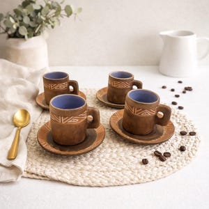 Może przedstawiać: Cztery brązowe ceramiczne filiżanki do espresso i spodki z białym geometrycznym wzorem. Wnętrze filiżanek jest niebieskie. Filiżanki i spodki ułożone są na plecionym podkładzie.