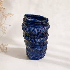 May include: A cylindrical ceramic vase with a deep cobalt blue glaze. The surface features a series of horizontal, raised, bumpy textures and organic, uneven ridges that wrap around the body, creating a tactile and irregular appearance.