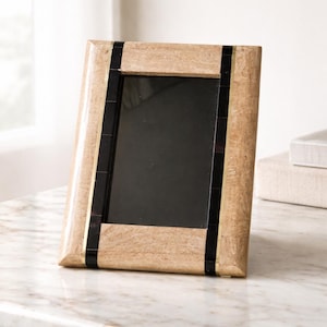 Peut inclure: Un cadre photo rectangulaire avec une finition marron clair texturée. Le cadre a des accents noirs et dorés sur les côtés. Le cadre est conçu pour contenir une photographie et est exposé sur une surface en marbre.