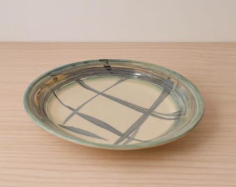 May include: Oval ceramic serving platter with a pale yellow interior and a crisscross pattern of gray lines. The rim is a mix of blue, green, and brown. A decorative piece for serving food.