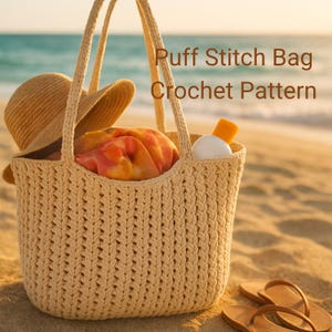 Könnte beinhalten: Eine beige gehäkelte Puff-Stich-Tasche mit Henkeln, gefüllt mit einem Strohhut, einem bunten Handtuch und Sonnencreme. Die Tasche befindet sich an einem Sandstrand mit Flip-Flops im Vordergrund. Der Text auf dem Bild lautet "Puff Stitch Bag Crochet Pattern."