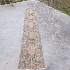 May include: A long, narrow runner rug featuring a repeating pattern of beige hexagonal medallions centered within dark gray and muted brown floral borders. The textile displays a weathered, low-pile texture with intricate geometric and botanical motifs.
