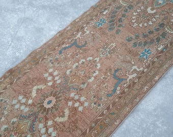 May include: A rectangular, vintage-style rug with a faded, distressed appearance. The rug features a central floral pattern in shades of peach, cream, and blue, with a dark brown border. The rug's design suggests it is a runner, suitable for hallways or entryways.