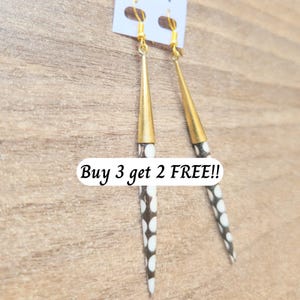 May include: A pair of dangle earrings with gold-colored conical tops and elongated, speckled white and brown bodies. The earrings hang from gold-colored hooks. The text "Buy 3 get 2 FREE!!" is visible.