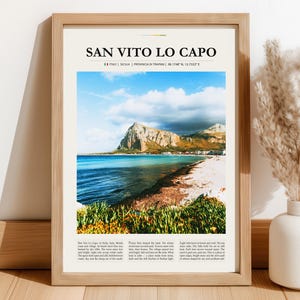 Op de afbeelding: Een ingelijste print met een kustlandschap en de tekst "SAN VITO LO CAPO". De afbeelding toont een strand met turquoise water, een berg en een bewolkte lucht. De lijst is lichtbruin.