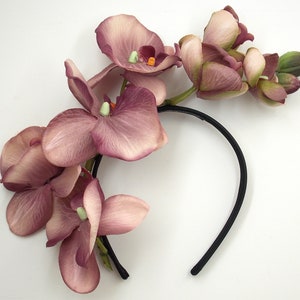 May include: A black headband with a cluster of pink orchid flowers attached. The flowers are arranged in a cascading design.