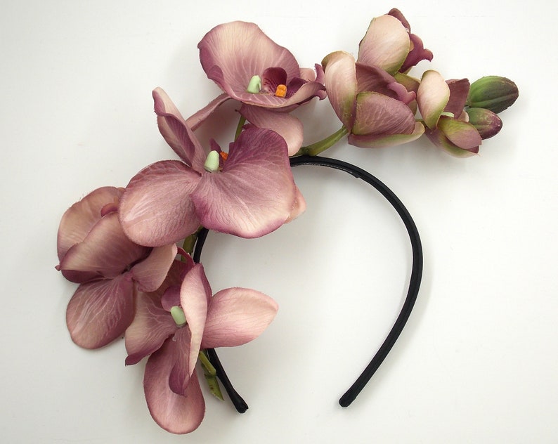 May include: A black headband with a cluster of pink orchid flowers attached. The flowers are arranged in a cascading design.