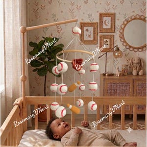 May include: A baby mobile featuring crocheted baseballs, a brown baseball glove, and yellow bats suspended from a circular wooden frame. The mobile hangs above a wooden crib, with white strings connecting the various sports-themed items.