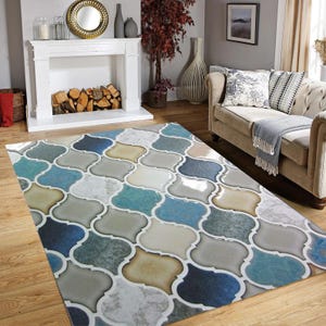 May include: A patterned area rug with a quatrefoil design in shades of blue, gray, and beige. The rug is placed on a hardwood floor in a living room setting. The rug's design is a repeating pattern of interlocking shapes.