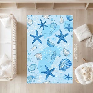 May include: A blue and white patterned rug featuring starfish and seashells. The rug has a light blue background with scattered blue starfish and white seashells. The design is reminiscent of a beach or ocean theme.