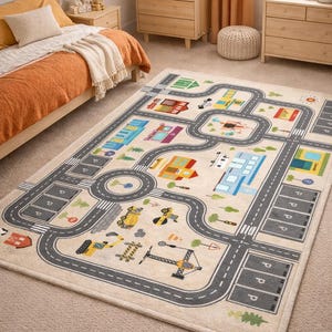 Puede incluir: Una alfombra rectangular beige con un diseño colorido de ciudad y carretera. La alfombra presenta carreteras grises, plazas de aparcamiento e ilustraciones de edificios, vehículos y árboles. La alfombra está colocada sobre una alfombra marrón claro.