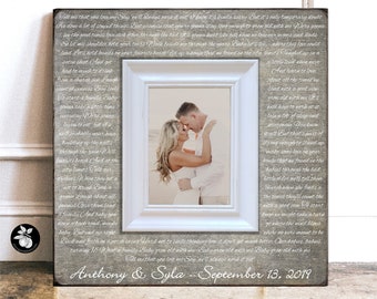 May include: A framed photo with a white border, featuring a couple embracing. The frame is set against a gray, textured background with handwritten text. The text includes the names "Anthony & Syla" and the date "September 13, 2019".