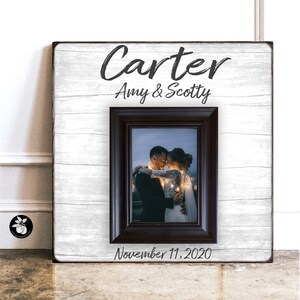 May include: A white wood picture frame with a black frame inside. The frame has the text "Carter Amy & Scotty" and "November 11, 2020" on it. A black and white photo of a couple is inside the frame.