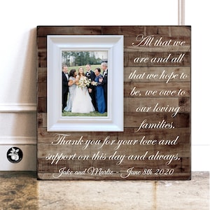 May include: A rustic wooden frame with a white mat and a photo of a wedding party. The frame has a white inscription that reads "All that we are and all that we hope to be, we owe to our loving families. Thank you for your love and support on this day and always. Jake and Marlic - June 8th 2020"