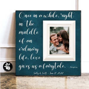 May include: A teal blue picture frame with a white mat and a white inner frame. The frame has a quote that reads "Once in a while, right in the middle of an ordinary life, love gives us a fairytale." The quote is attributed to "Anonymous" and the date "June 17, 2022" is written below. The frame has a photo of a couple in the inner frame.