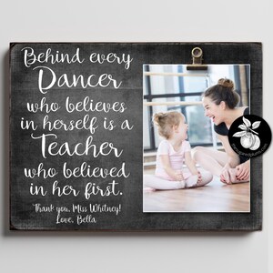 May include: A framed wooden sign with a photo of a dancer and teacher. The sign has the text "Behind every Dancer who believes in herself is a Teacher who believed in her first." The photo is held by a gold clip.