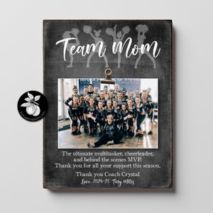May include: A black chalkboard sign with a photo frame and the text "Team Mom". The photo frame has a picture of a group of cheerleaders and their coach. The text below the photo reads "The ultimate multitasker, cheerleader, and behind the scenes MVP. Thank you for all your support this season. Thank you Coach Crystal Love. 2024-25 Tiny Mites"