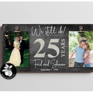 Könnte beinhalten: Ein schwarzer Schiefer-Bilderrahmen mit zwei Clips zum Halten von Fotos. Der Rahmen trägt den Text "We still do! 25 YEARS Fred and Sharon September 7, 1994". Der Rahmen enthält zwei Fotos, eines von einem Paar an ihrem Hochzeitstag und eines vom selben Paar in der heutigen Zeit.