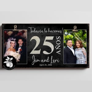 May include: A rectangular black wooden sign featuring two metal clips for holding photos. The text reads "Todavía lo hacemos! 25 AÑOS", "Jim and Lori", and "April 28, 2000". The number 25 is in a silver glitter finish, and the text is in white.