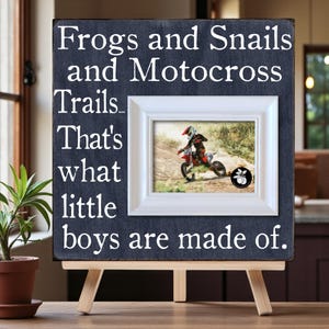 Puede incluir: Un letrero enmarcado con el texto "Frogs and Snails and Motocross Trails... That's what little boys are made of." El letrero tiene una foto enmarcada en blanco de una persona montando una moto de cross.