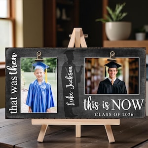 May include: A graduation photo frame on a wooden easel. The frame is black with white text that says "that was then" and "this is NOW CLASS OF 2026". It holds two photos and a silhouette of a graduate with the name "Luke Jackson".