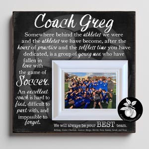 以下が含まれることがあります： 黒い背景にサッカーボールのグラフィックと「Coach Greg」という白い文字が書かれた正方形の木製プレート。コーチとチームへのメッセージが添えられています。白いフレームには、フィールド上のサッカーチームの写真が収められています。