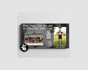 May include: A rectangular wooden photo display board with a dark gray soccer ball pattern background. It features the text "What feels like the end is often the beginning," "#45," "MARY SMITH," and "Class of 2025." Two metal clips hold photos.