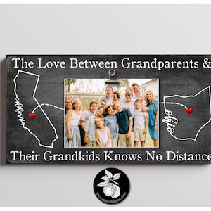 May include: A black and white sign with the text "The Love Between Grandparents & Their Grandkids Knows No Distance". The sign features a map of California and Ohio with a red heart in each state. A photo of a family is in the center of the sign.