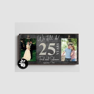 May include: A rectangular dark gray wooden photo display board featuring two metal clips holding photographs. The text reads We still do! 25 YEARS Fred and Sharon September 7, 1994. The board displays a wedding photo on the left and a couple on the right.