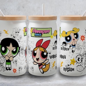 Puede incluir: Tres vasos de vidrio blancos con tapas de bambú y pajitas blancas. Cada vaso presenta un personaje diferente de las Powerpuff Girls: Pétalo, Burbuja y Cactus. El logotipo de las Powerpuff Girls también es visible.