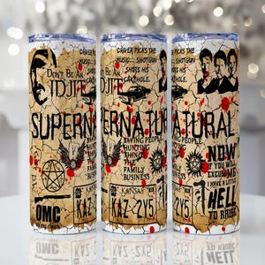 Puede incluir: Tres vasos de acero inoxidable con un diseño desgastado con texto y gráficos del programa de televisión Supernatural. El diseño incluye imágenes de personajes, símbolos y frases sobre un fondo beige con salpicaduras rojas.