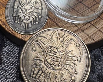 May include: Three metal coins featuring a grinning jester design. The coins are in varying shades of bronze and silver, with intricate details in the jester's face and costume. One coin is in a clear plastic case.
