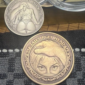 May include: Two round, metallic coins with detailed relief designs. One coin features a woman's backside with the text "HEADS I GET TAIL". The other coin shows a woman's eyes and a hand with the text "TAILS I GET HEAD".